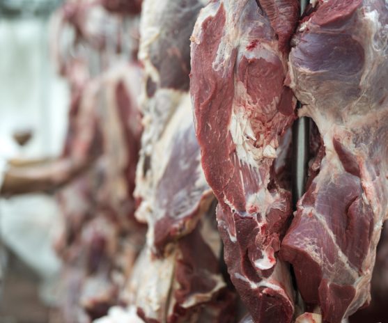 fresh red meet and butchery worker working in background.